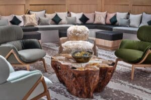RAKxa spa lounge at The St. Regis Aspen featuring a live-edge petrified wood coffee table, velvet lounge chairs in sage and forest green, and a curved banquette with layered pillows designed by