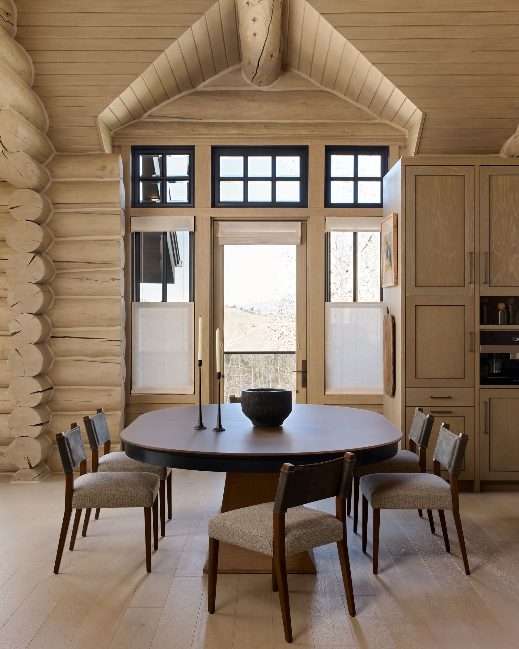 Dining room with round dark table, upholstered chairs, bleached log walls, and mountain views, Snowmass Colorado