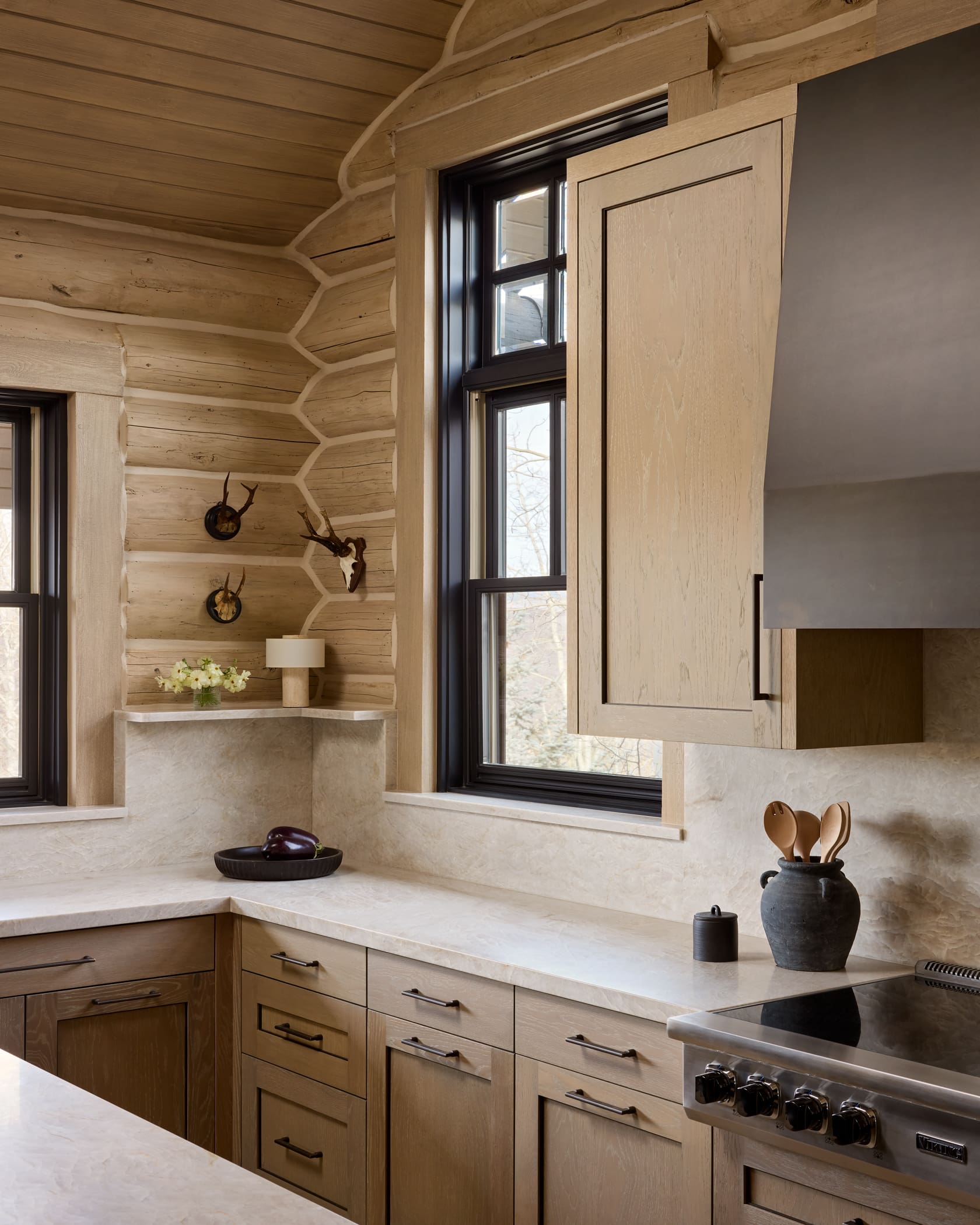 Kitchen corner with bleached log walls, stone countertops, antler mounts, and professional range, Snowmass cabin remodel