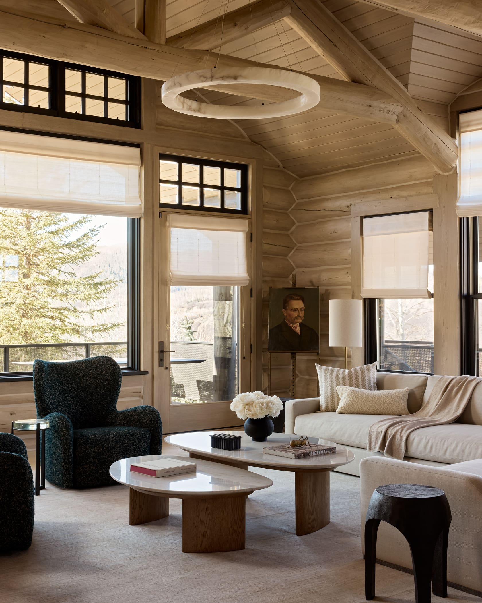 Living room with alabaster ring pendant, bleached log walls, teal boucle chair, and travertine tables, Snowmass Colorado
