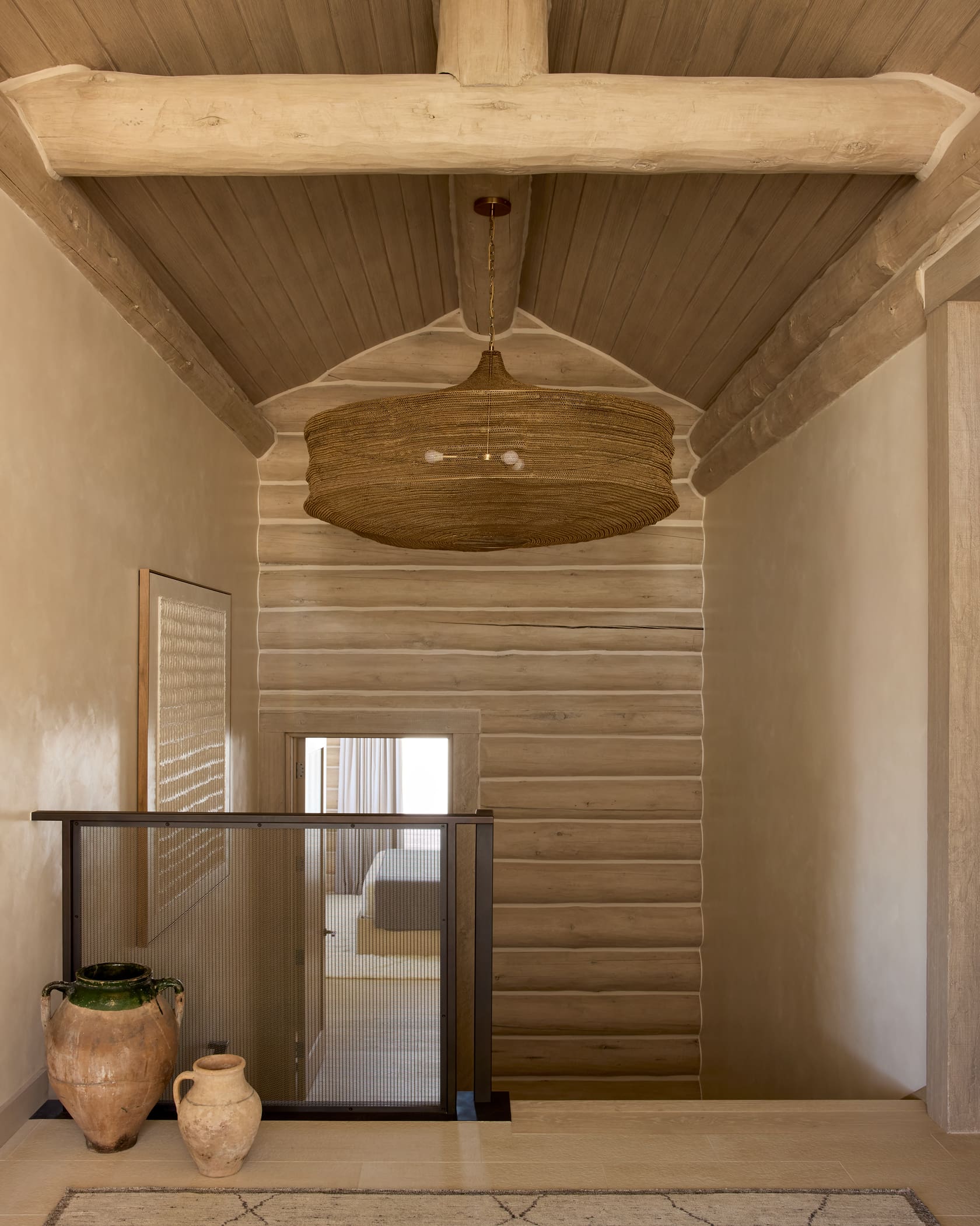 Stair landing with woven drum pendant, bleached log walls, ribbed glass guardrail, and antique pottery, Snowmass Colorado