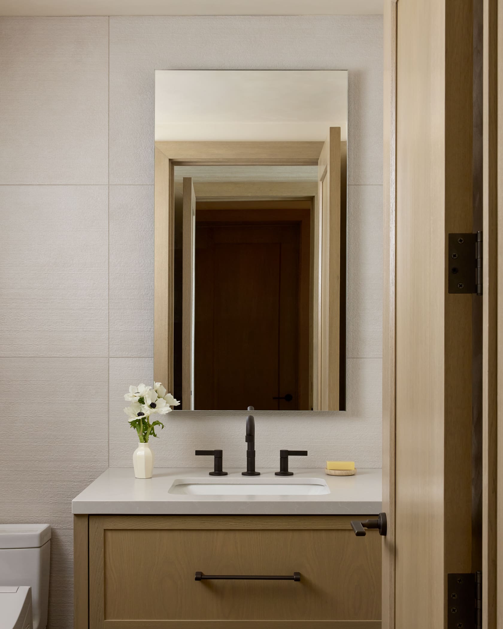Guest bathroom with textured tile walls, oak-framed mirror, stone vanity, and black fixtures, Snowmass log cabin remodel